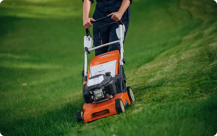 Person pushing an orange gas mower across a green slope for West End Vancouver lawn mowing
