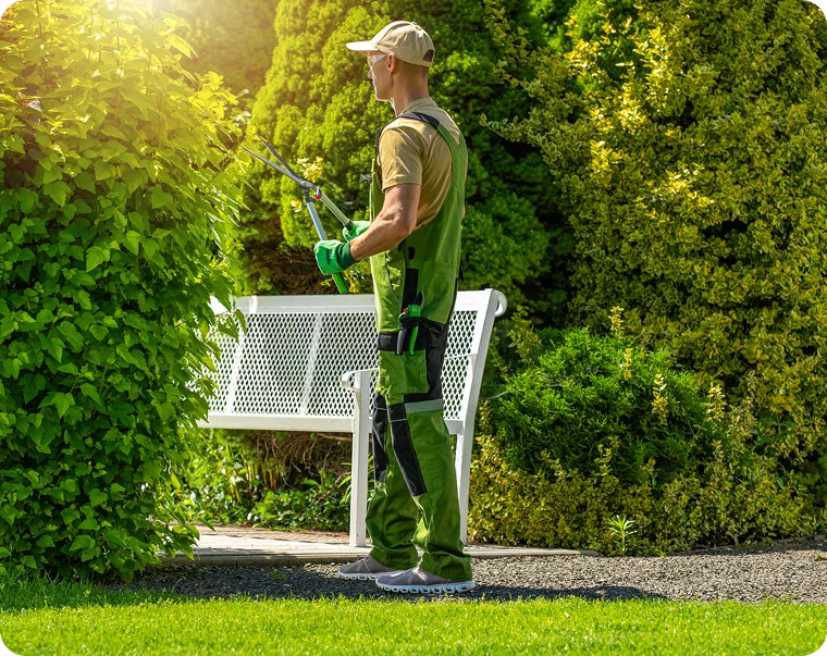 Gardener with a hedge trimmer beside a white bench, lawn care for multi-unit apartment buildings in Vancouver