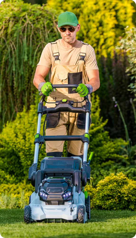 Gardener in overalls pushing a cordless mower through a garden for rental property lawn care in Vancouver
