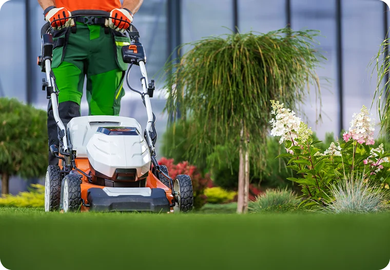 Battery mower cutting a courtyard lawn beside garden beds for strata lawn care in Vancouver