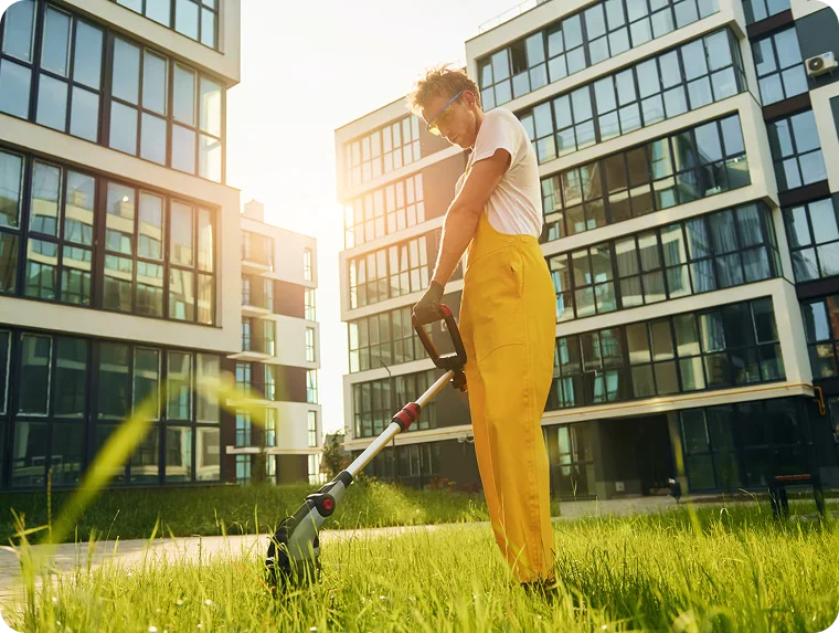 Landscaper using a string trimmer on grass between modern condo towers for strata lawn care in Vancouver