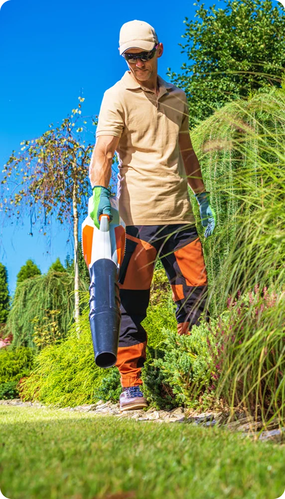 Landscaper carrying a leaf blower along a garden path, lawn care for multi-unit apartment buildings in Vancouver